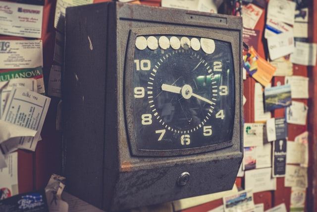 A time clock on a bulletin board with notes pinned to it.